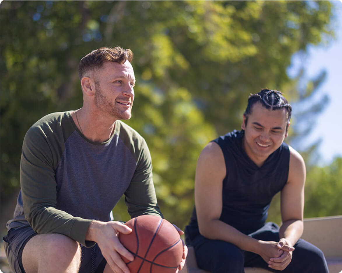 Two men on a bench.  One man is holding a basketball.